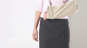 A woman stands with her left arm in a sling.