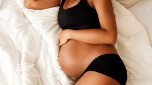 A pregnant woman lies on her side in bed.