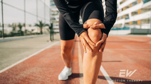 A runner on a track grips their knee in pain. [Anna Ostenina, Getty Images via Canva.com]