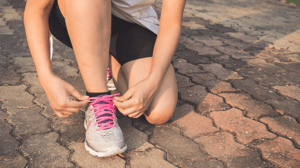 A person kneels on the ground to tie their shoe.