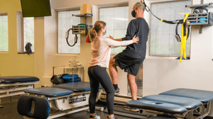 A woman coaches a man lifting his left leg.