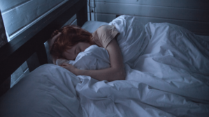 A woman lays in bed in a dark room.
