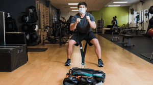 A man drags a weighted bag across the floor with his waist.