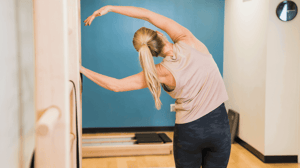 A woman bends to her left side with her arm over her head.