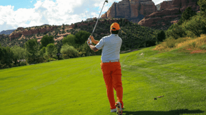 From behind, a golfer watches his swing.