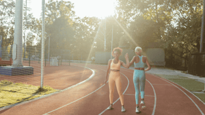 Two women high-five while they walk around a track.