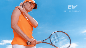 A lady holds her right shoulder in pain, while holding a tennis raquet.