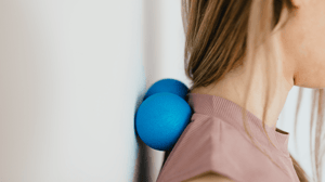 A woman uses balls up against a wall to relieve tension in her neck.