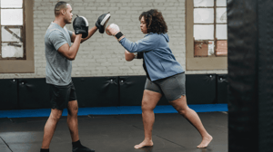 A woman boxes with a male instructor.