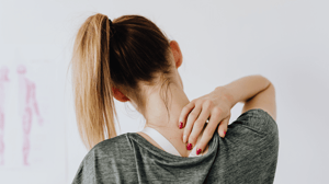 A woman touches her upper back between her shoulders.