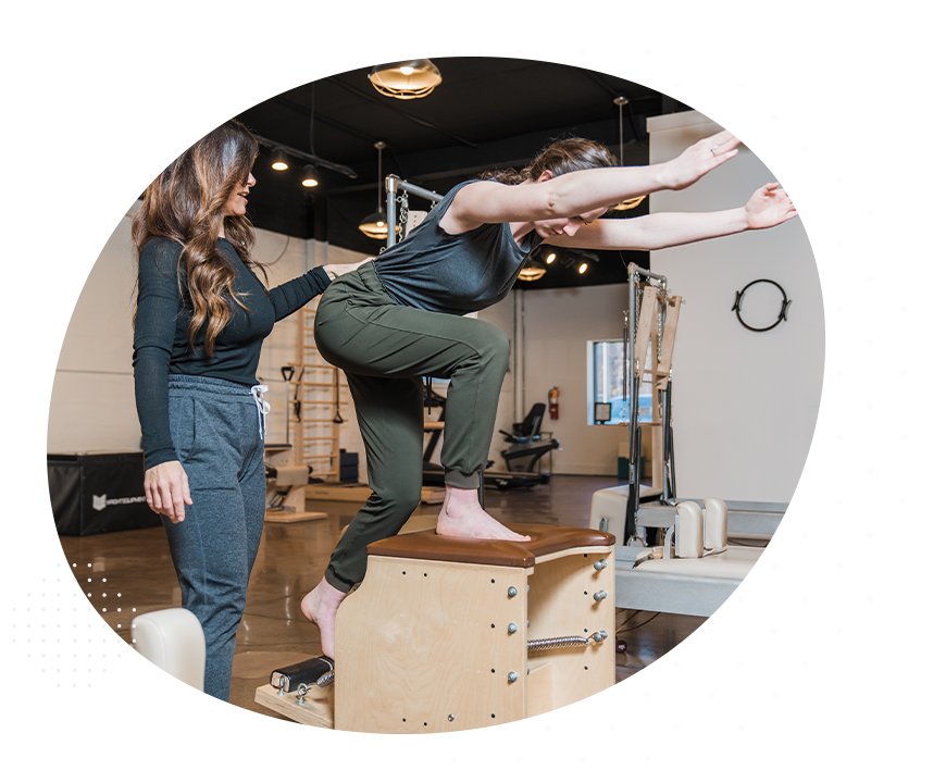 Girl standing on pilates equipment with instructors support