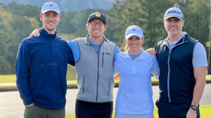 Four people stand together on a golf course. 