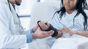 A doctor fits a wrist brace on a woman in a hospital bed.
