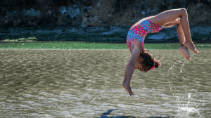 A young girl does a back handspring over a river.