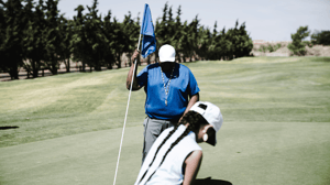 A young female golfer lines up a put as her coach watches.