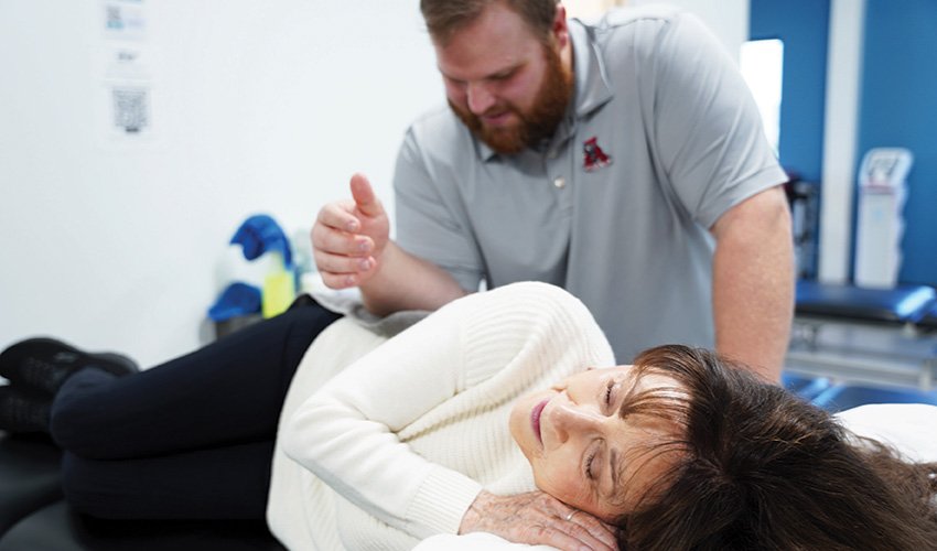 Physical therapist performing manual therapy on a patient lying on a treatment table.